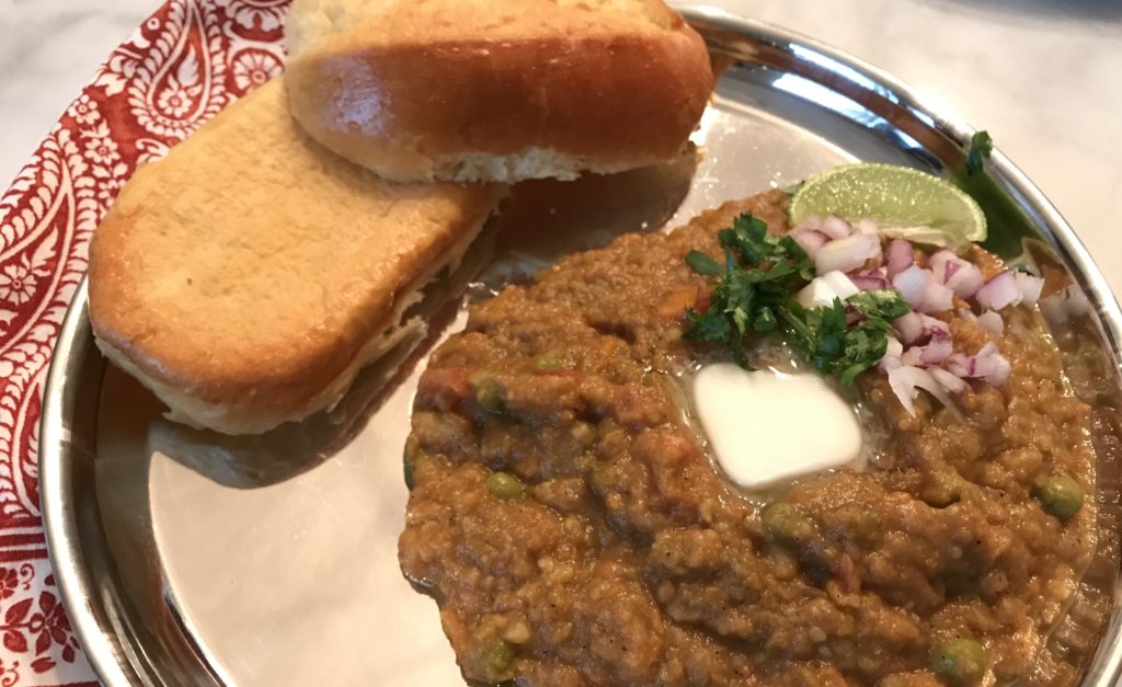 pau pav bhaji with toasted rolls, and garnished with butter, red onions and cilantro, on a traditional indian metal plate