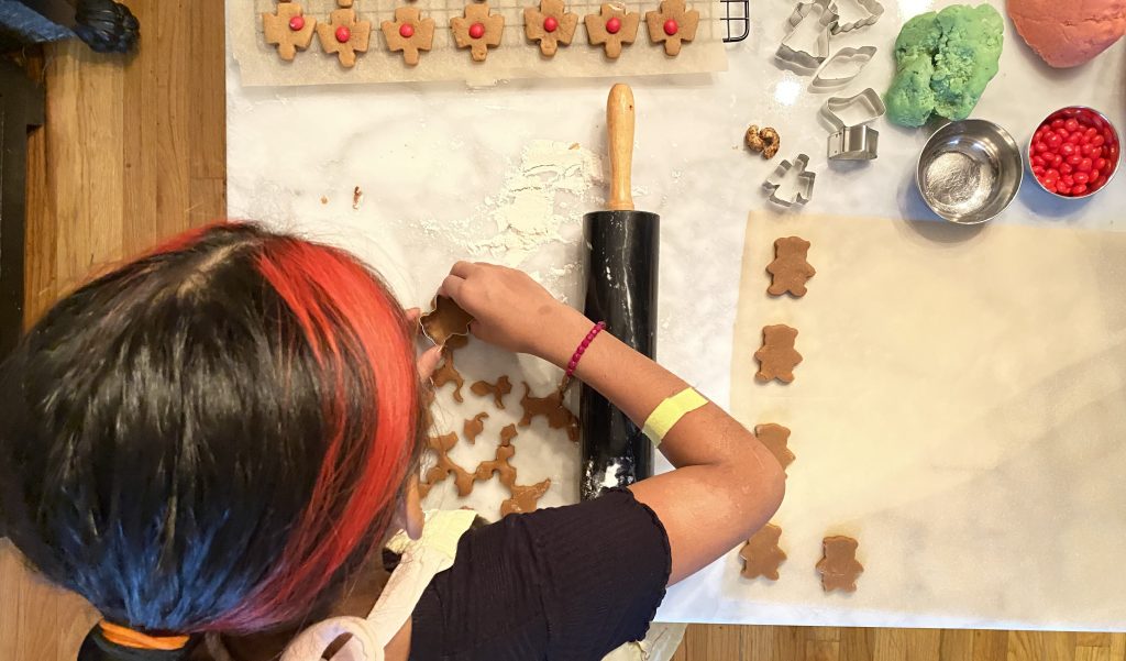 apprentice helping to make gingerbread mini cookies in the shape of bears and angels, with red hot candies for hearts