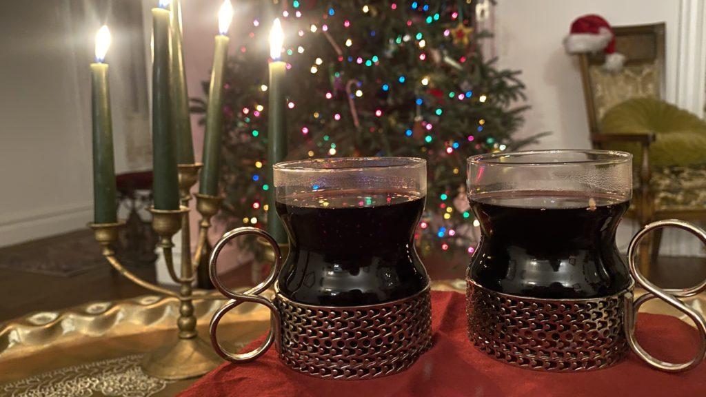 finnish glögi in a pair of tsaikke glasses in front of a lighted christmas tree and a pretty lit candle