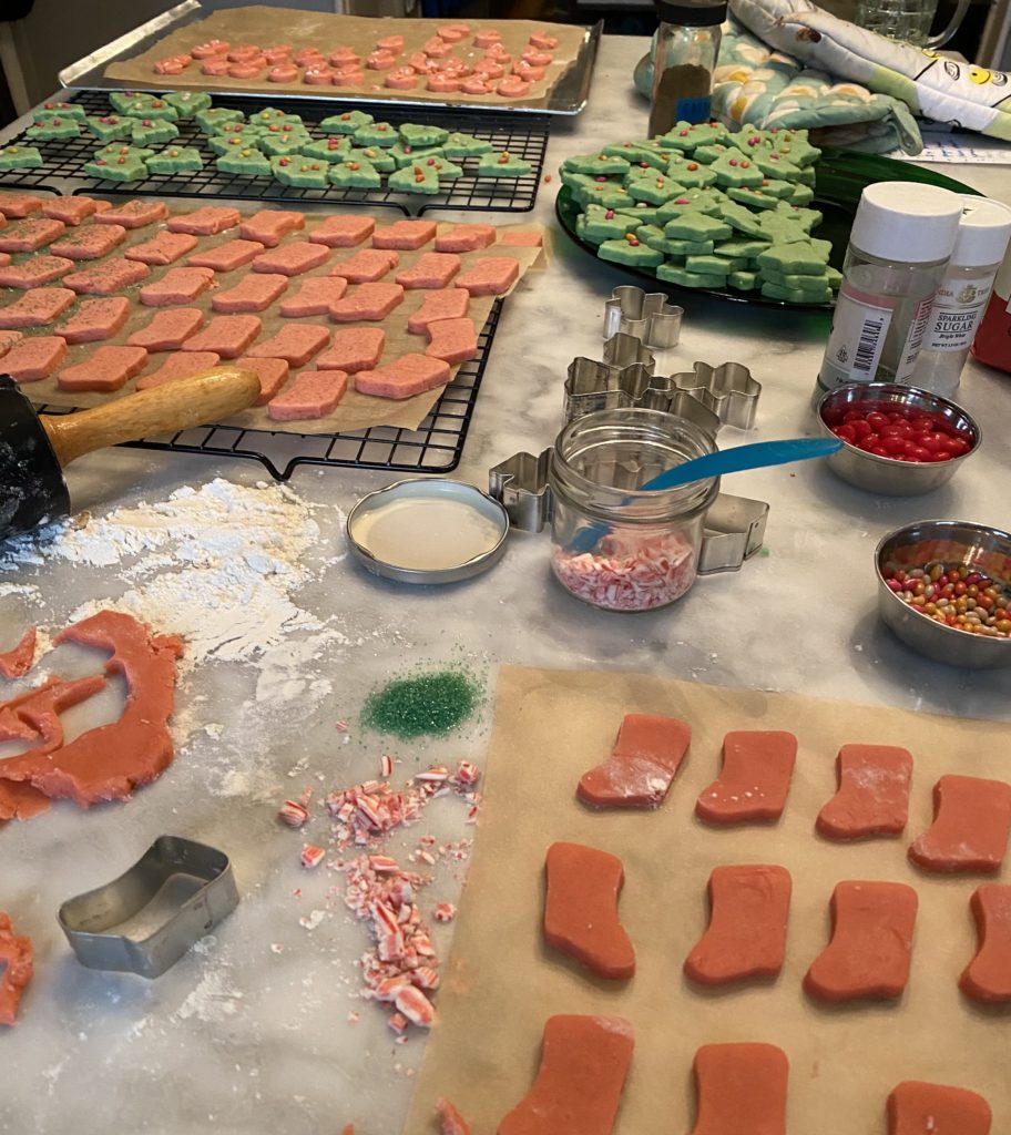 busy home kitchen whipping up christmas cookies to deliver to friends during the covid pandemic.  red and green almondy cookies and candy cane. 